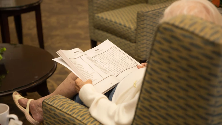 Senior seated in a chair with a crossword puzzle